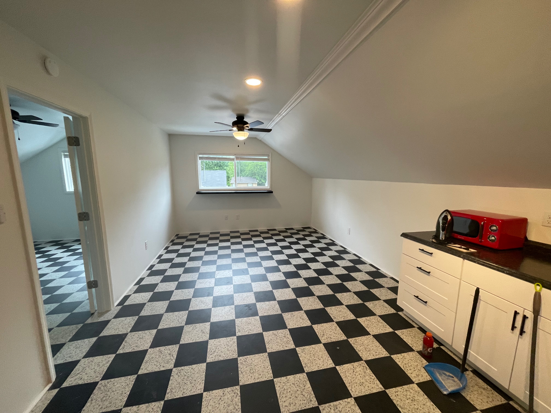 Bright open studio living area with vaulted ceiling, ceiling fan, and signature checkered floor